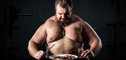 Shirtless muscular man eating a nutritious meal, symbolizing strength and health.