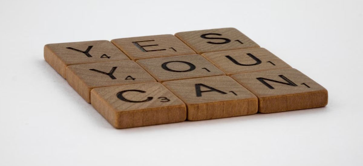 Wooden Scrabble tiles spelling 'Yes You Can' on a white background.