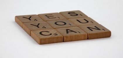 Wooden Scrabble tiles spelling 'Yes You Can' on a white background.