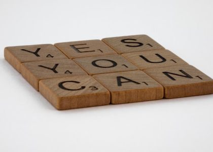 Wooden Scrabble tiles spelling 'Yes You Can' on a white background.